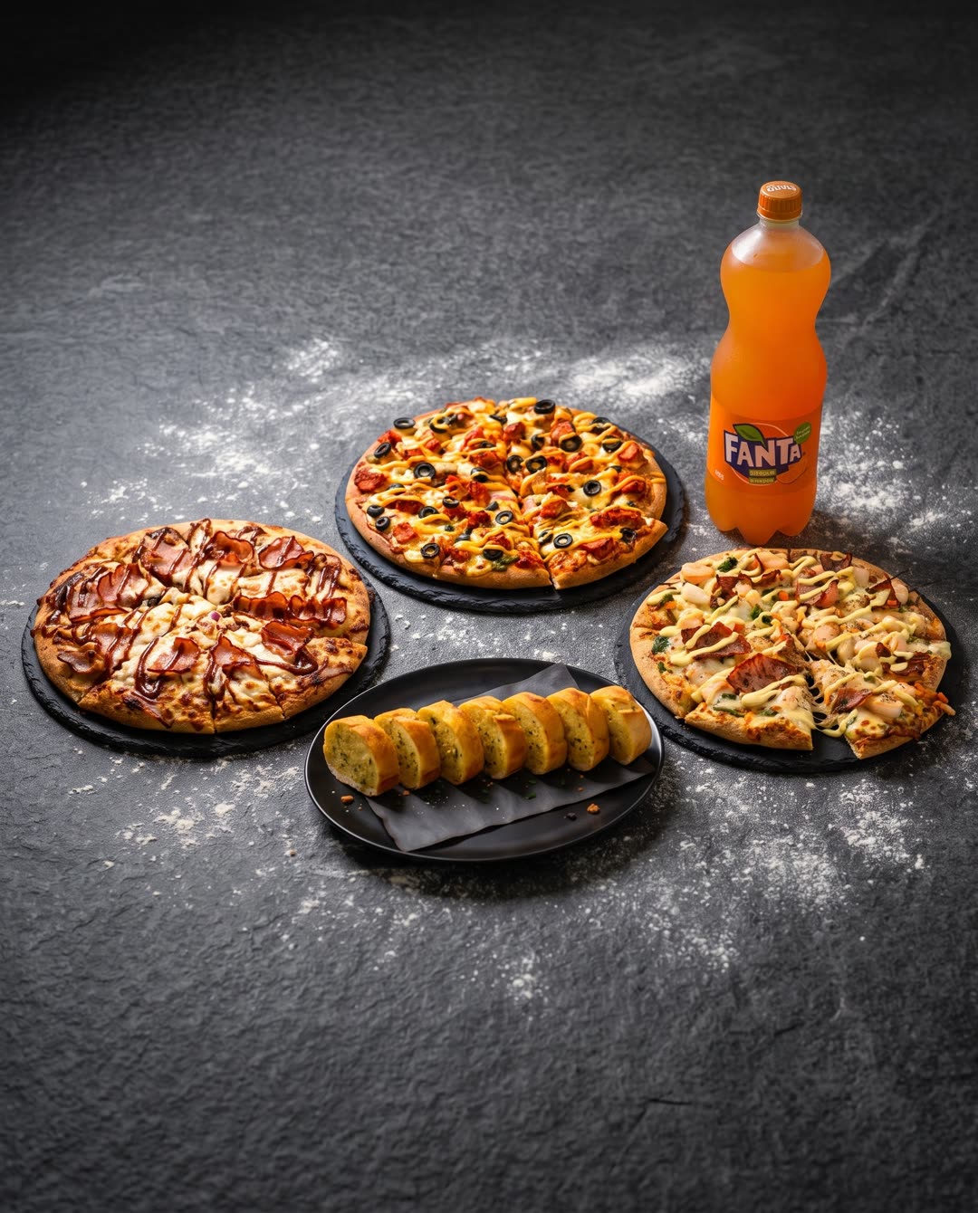 Three large pizzas, garlic bread and a 1.5L Fanta on dark stone